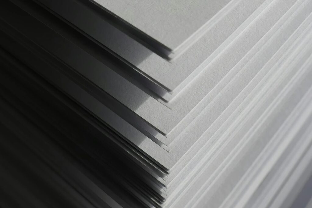 Artistic close-up of stacked white paper sheets creating geometric shadows and patterns in soft light.
