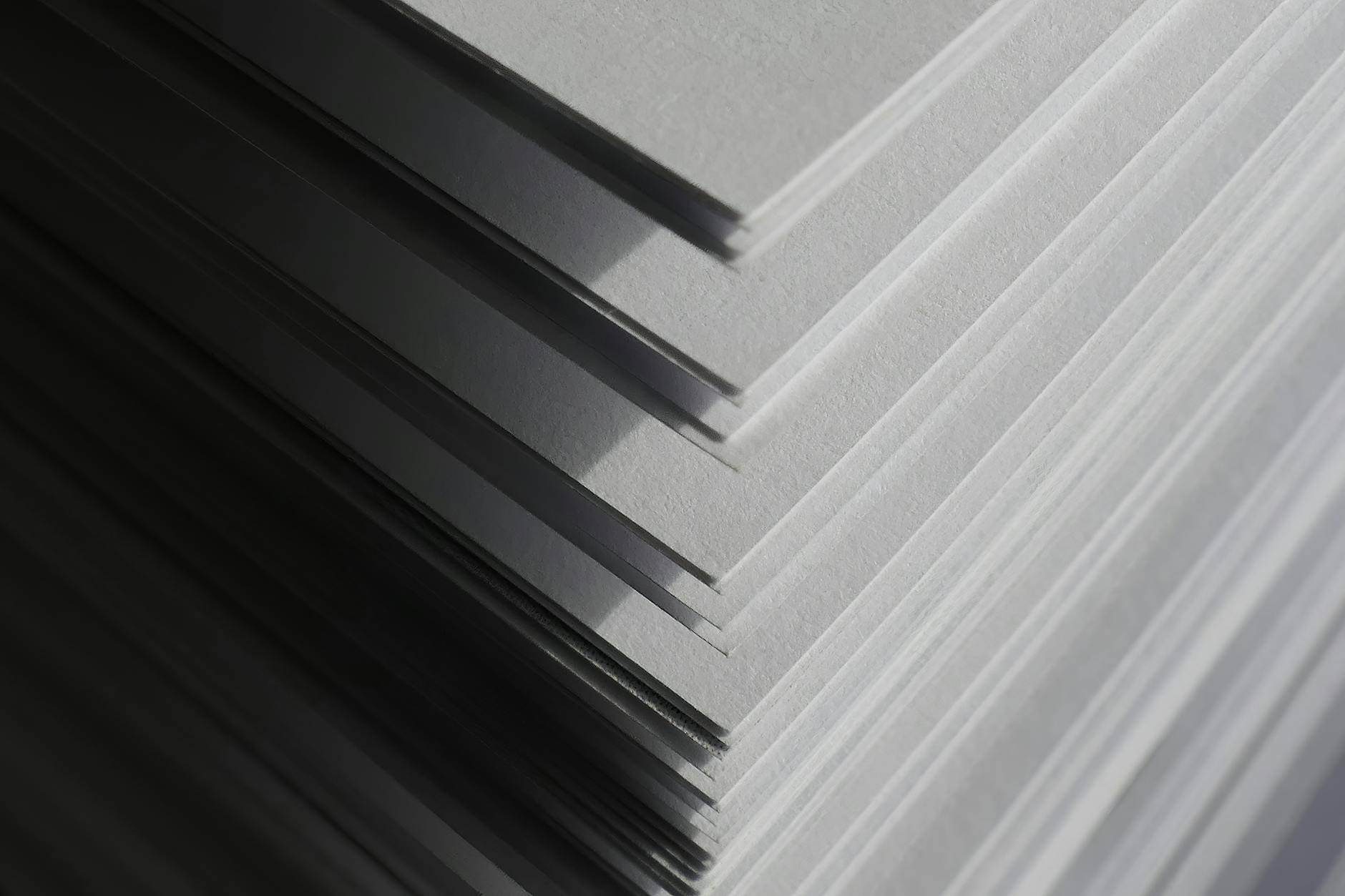 Artistic close-up of stacked white paper sheets creating geometric shadows and patterns in soft light.